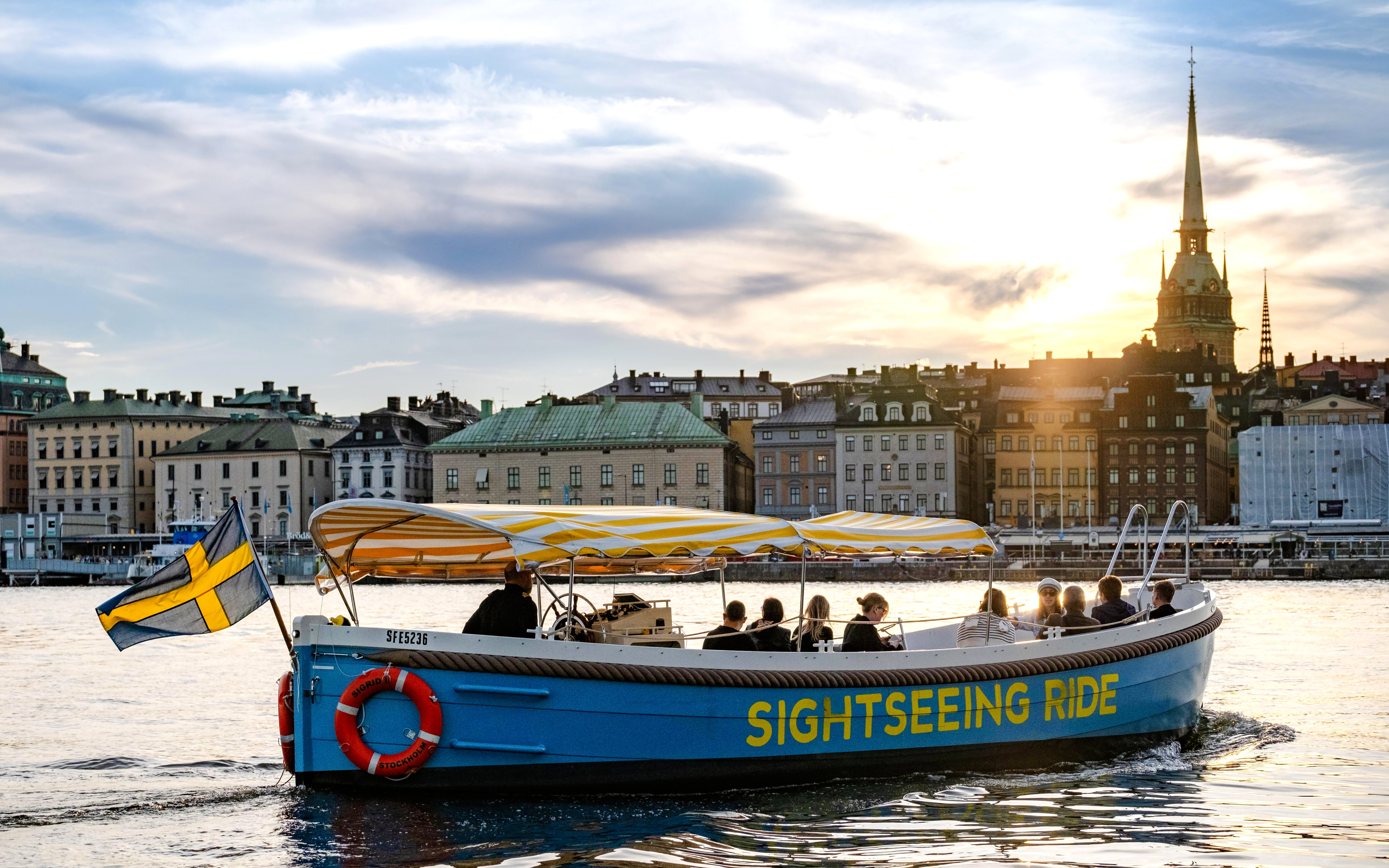 Sightseeing boat tour on Stockholm's waterfront with cityscape and sunset in the background.