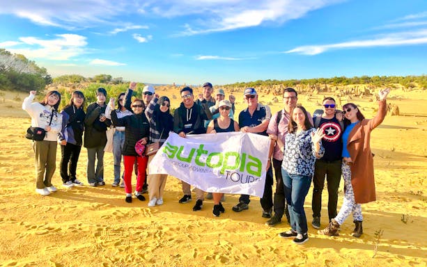 Tourists enjoying Pinnacles Desert during sunset tour with group banner.