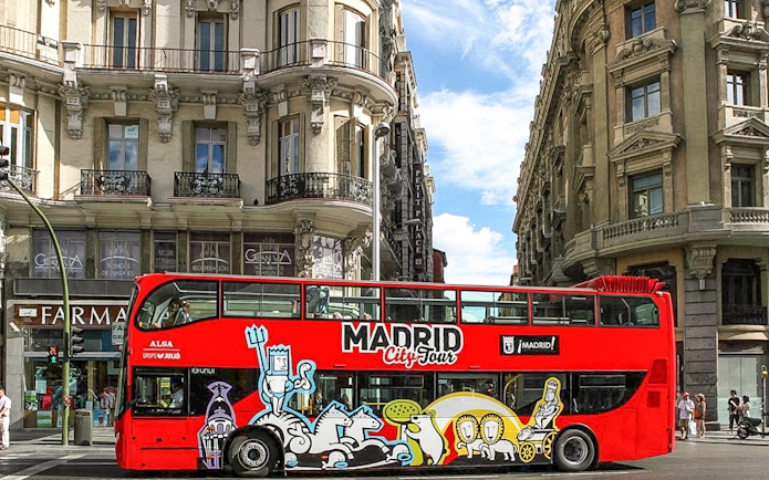 Madrid hop-on hop-off bus passing historic buildings on a sunny day.