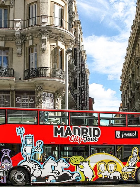 Madrid hop-on hop-off bus passing historic buildings on a sunny day.