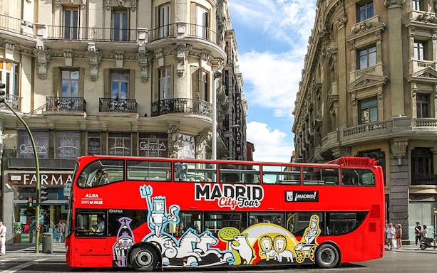 Madrid hop-on hop-off bus passing historic buildings on a sunny day.