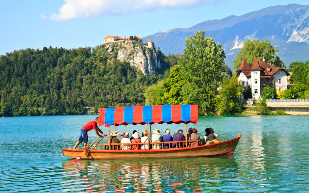 Tourists on a boat ride at Bled Lake with Bled Castle in the background.