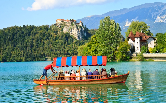Tourists on a boat ride at Bled Lake with Bled Castle in the background.
