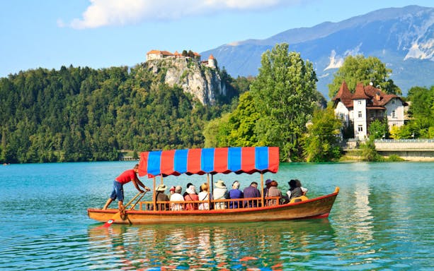 Tourists on a boat ride at Bled Lake with Bled Castle in the background.