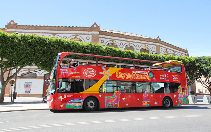 City Sightseeing HOHO bus in Malaga near historic building.