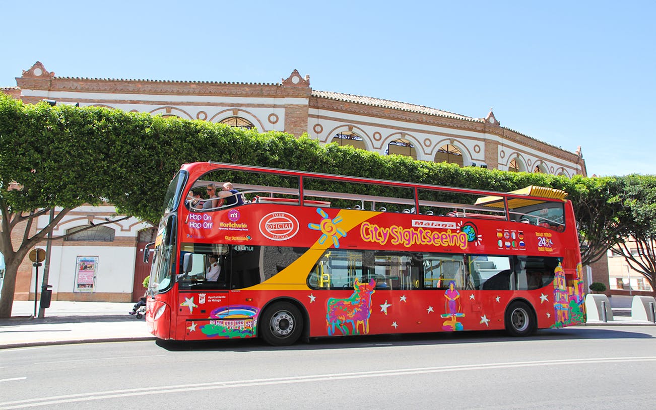 City Sightseeing HOHO bus in Malaga near historic building.