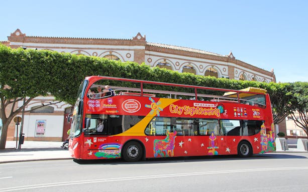 City Sightseeing HOHO bus in Malaga near historic building.