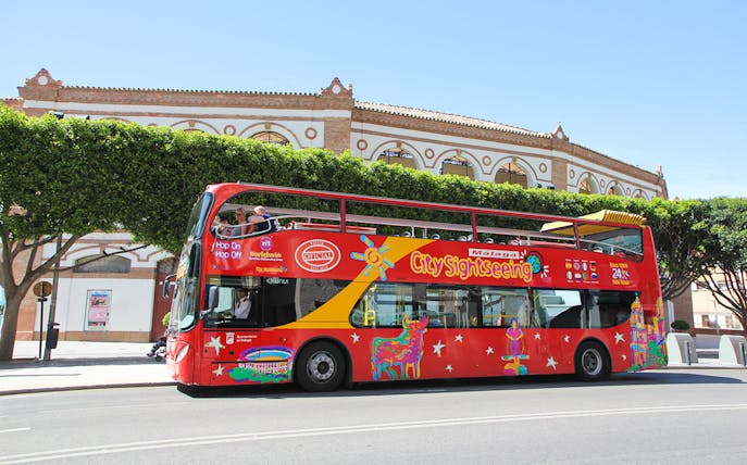 City Sightseeing HOHO bus in Malaga near historic building.