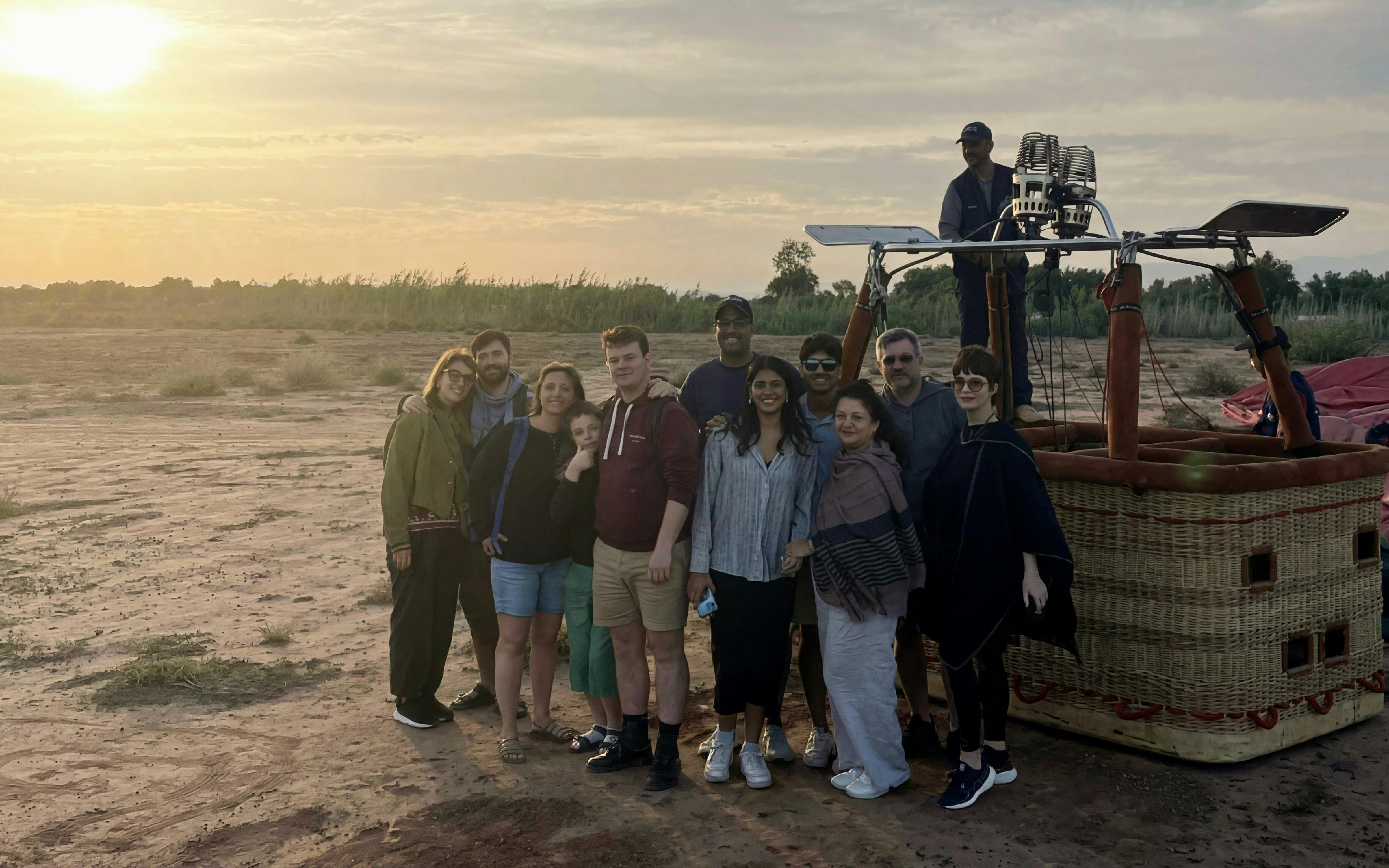 Group beside hot air balloon at sunrise in Marrakech desert.