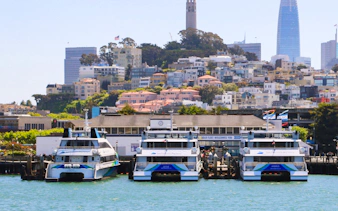 Boats docked at San Francisco Bay with cityscape and Coit Tower in the background.