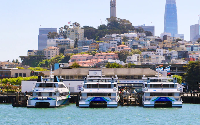 Boats docked at San Francisco Bay with cityscape and Coit Tower in the background.