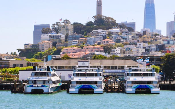 Boats docked at San Francisco Bay with cityscape and Coit Tower in the background.