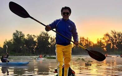 Kayaking at sunrise in Xochimilco canals with trees in the background.