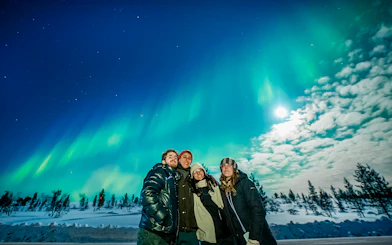 Group enjoying Northern Lights in Tromso with snowy landscape and clear sky.