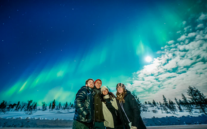 Group enjoying Northern Lights in Tromso with snowy landscape and clear sky.