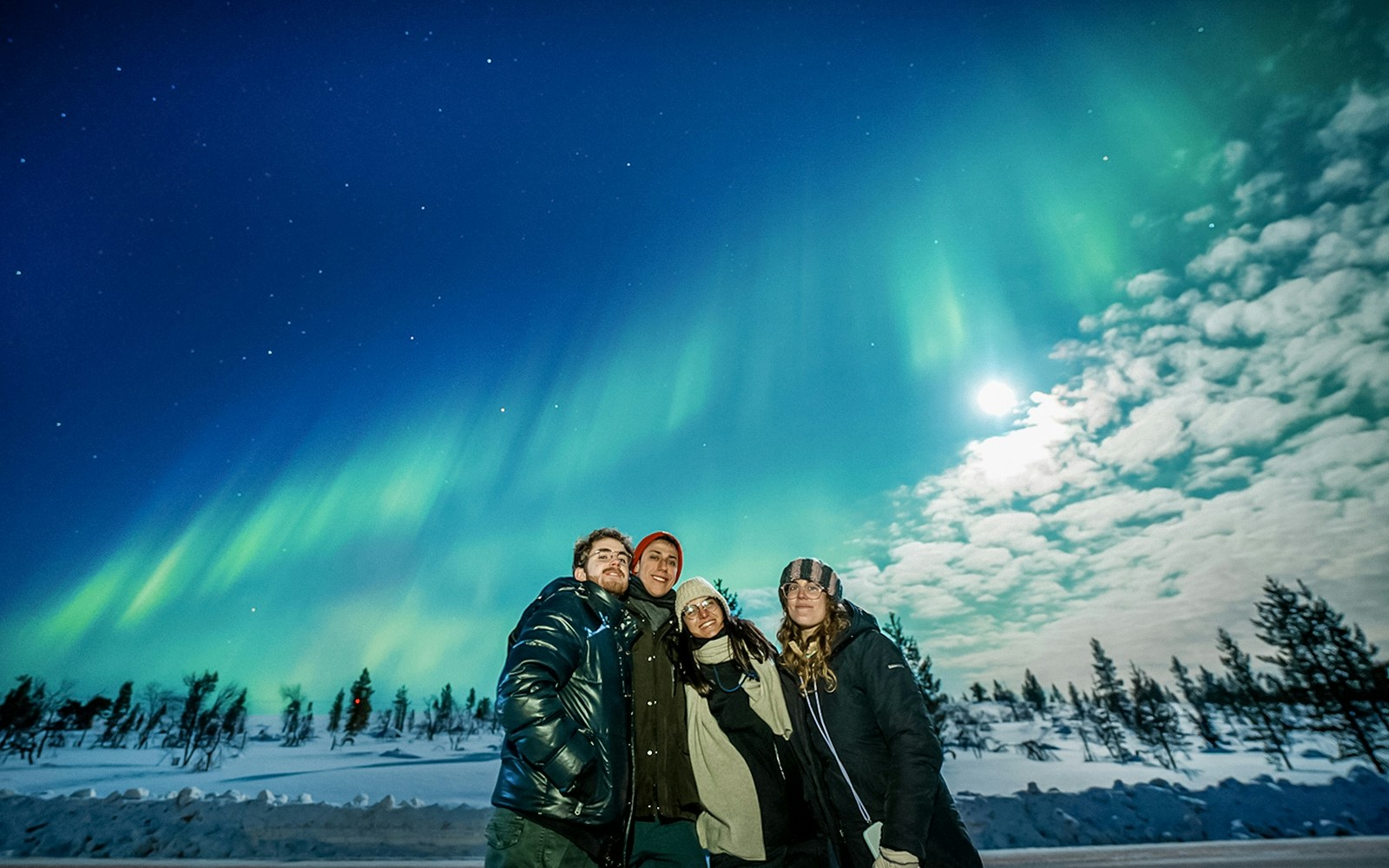 Group enjoying Northern Lights in Tromso with snowy landscape and clear sky.