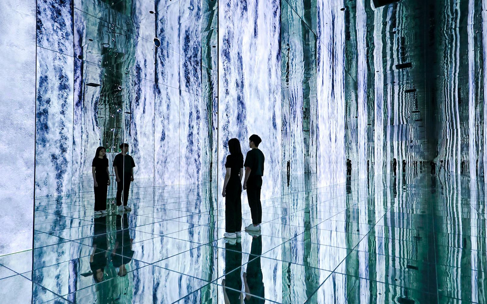Visitors at the 'Waterfall Infinite' installation, ARTE MUSEUM DUBAI, surrounded by mirrored walls.