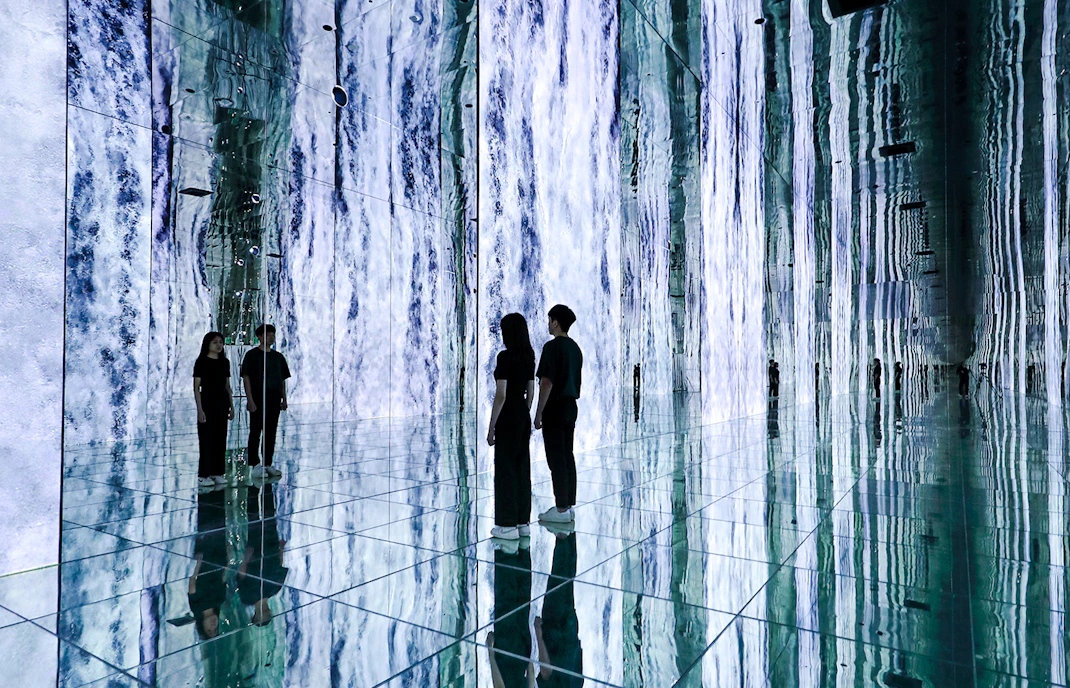 Visitors at the 'Waterfall Infinite' installation, ARTE MUSEUM DUBAI, surrounded by mirrored walls.