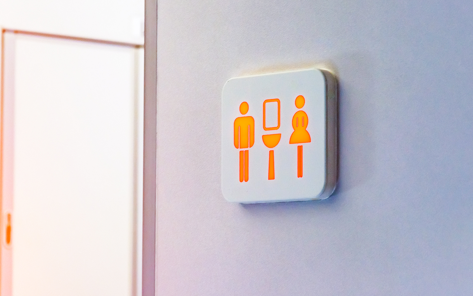 Restroom sign with male, female, and sink symbols illuminated on a wall.