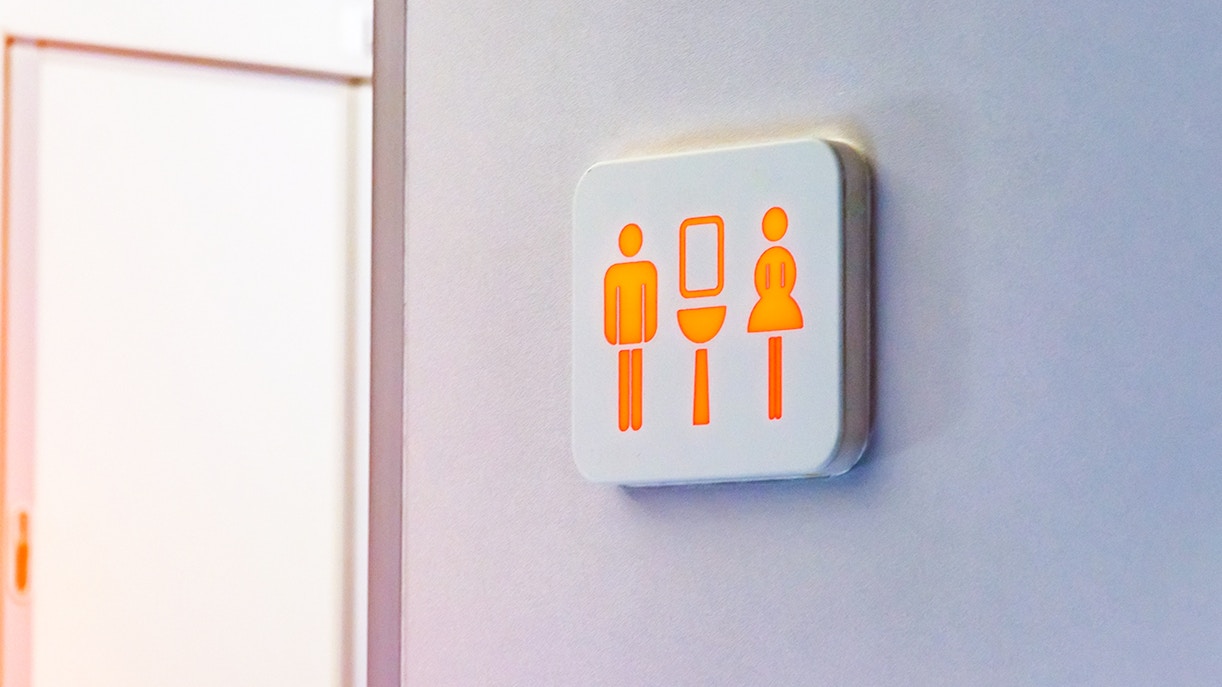 Restroom sign with male, female, and sink symbols illuminated on a wall.