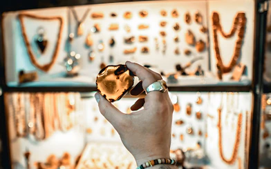 Hand holding amber piece in Gdańsk workshop with jewelry display in background.