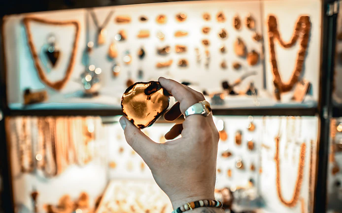 Hand holding amber piece in Gdańsk workshop with jewelry display in background.