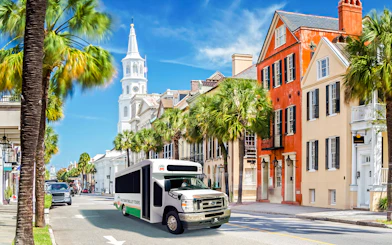 Charleston trolley passing historic colorful buildings and church steeple on city tour.