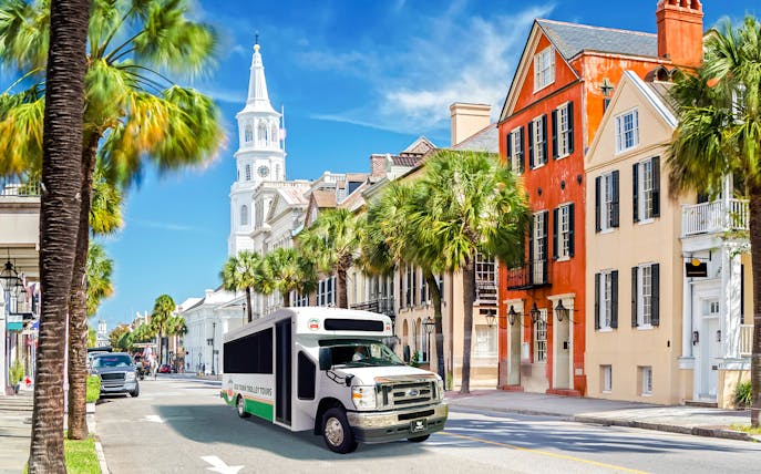 Charleston trolley passing historic colorful buildings and church steeple on city tour.