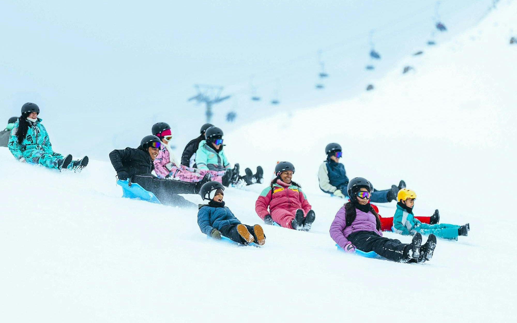 Tourists sledding down a snowy hill at Farellones Park, Chile.