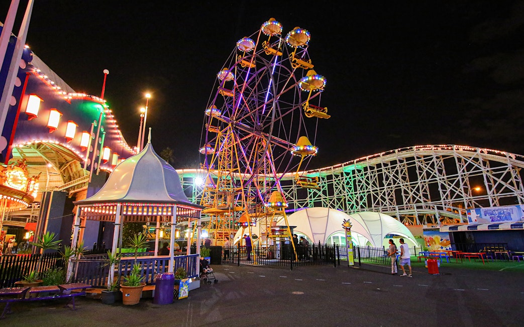 Ferris wheel illuminated at night in Luna Park, Melbourne, with roller coaster in background.