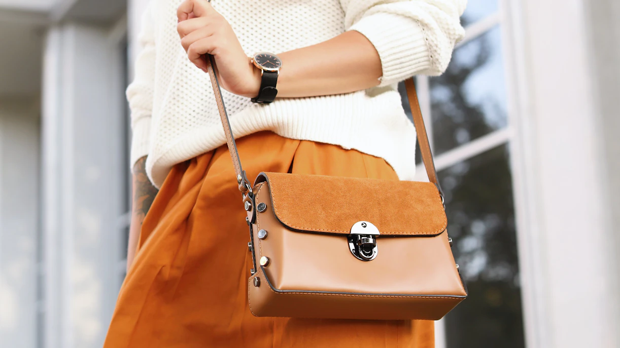 Woman holding a tan leather crossbody bag.