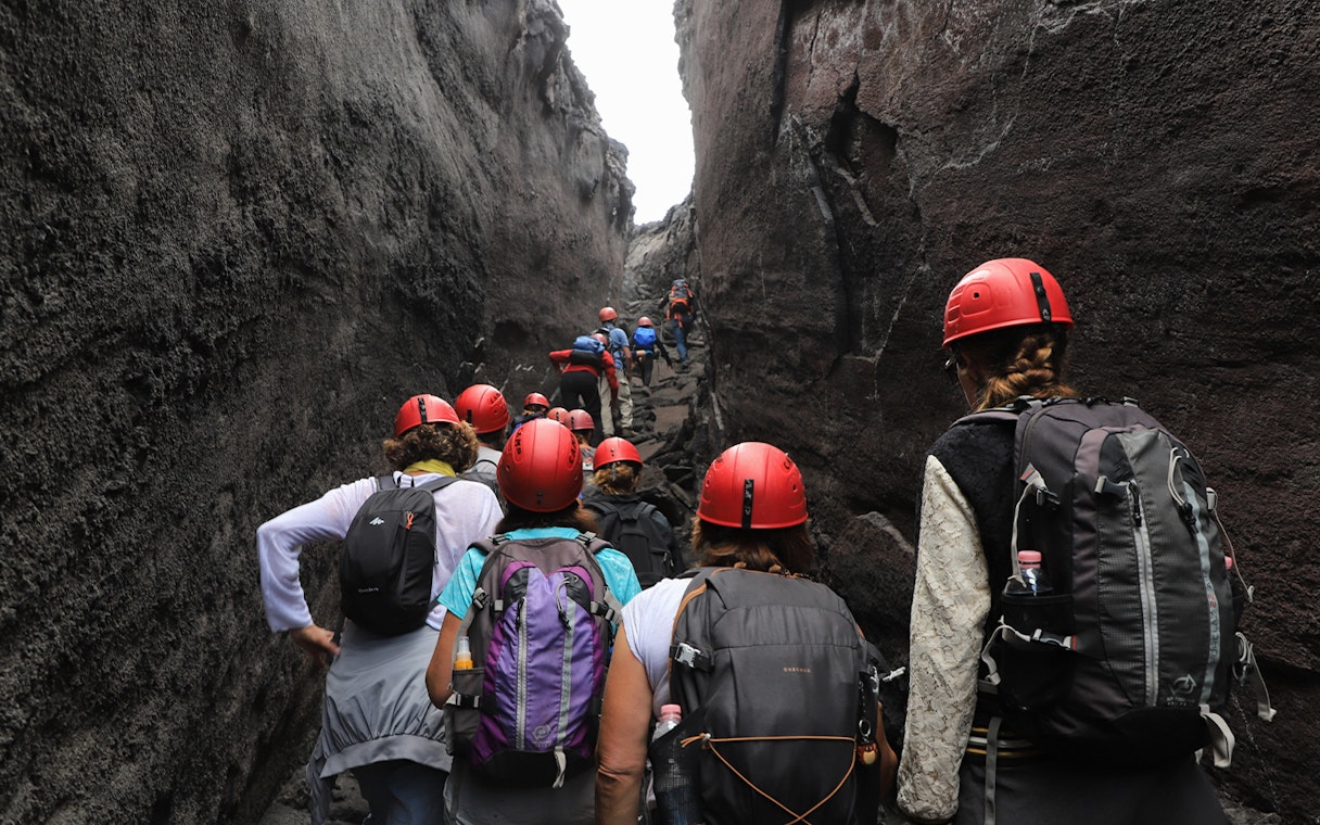 Hikers with helmets navigating narrow rocky path at Mount Etna.