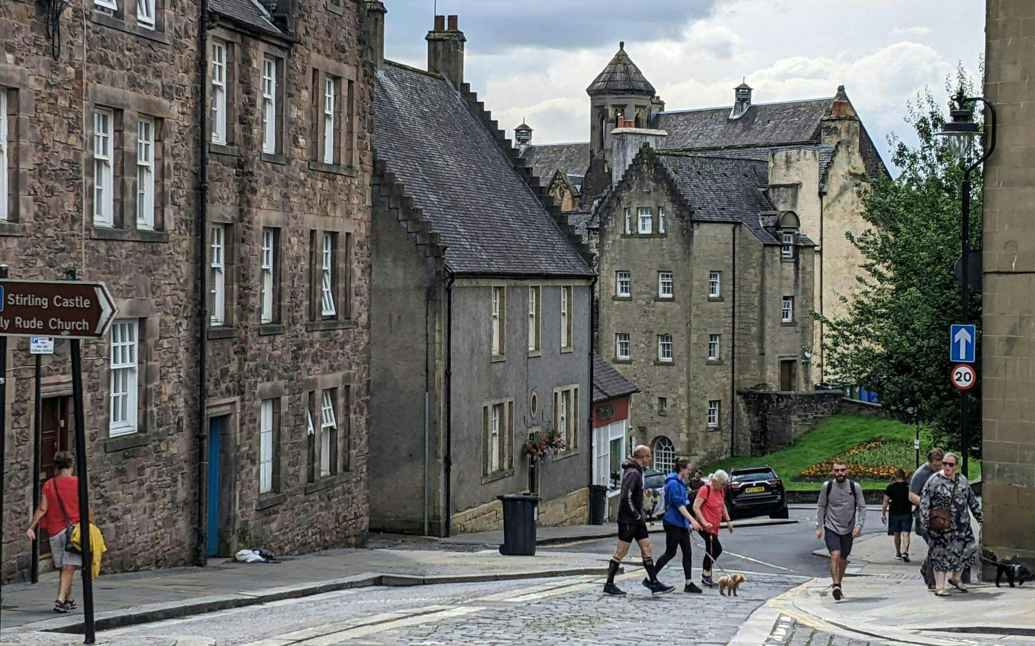 Pedestrians walking on Stirling road near historic stone buildings in Scotland.