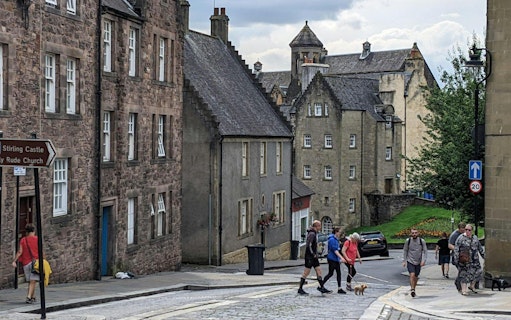 Pedestrians walking on Stirling road near historic stone buildings in Scotland.