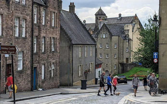Pedestrians walking on Stirling road near historic stone buildings in Scotland.
