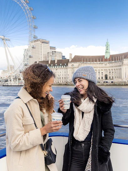 Two people enjoying a River Thames cruise with the London Eye in the background.
