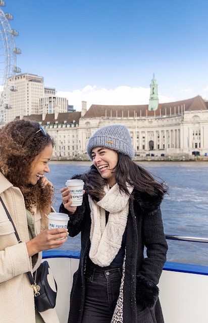 Two people enjoying a River Thames cruise with the London Eye in the background.