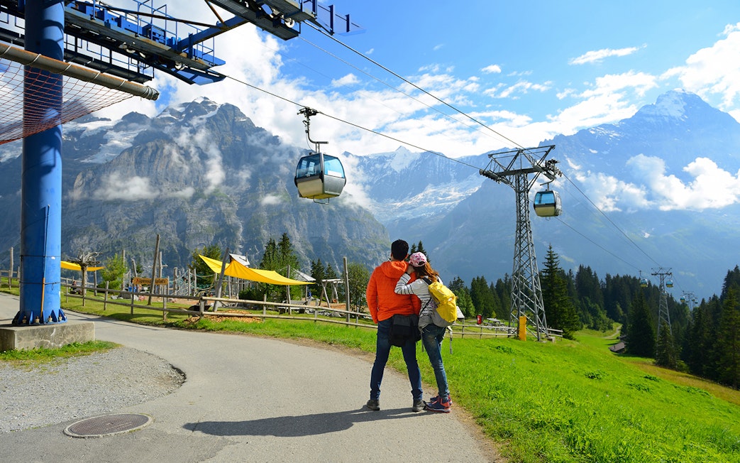 Couple embracing near cable cars at Grindelwald First, Switzerland, with mountain views.