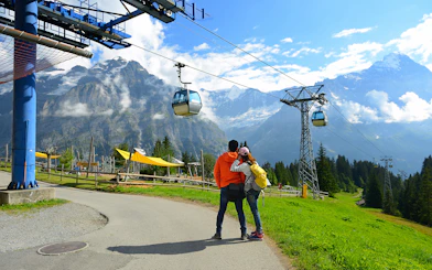 Couple embracing near cable cars at Grindelwald First, Switzerland, with mountain views.