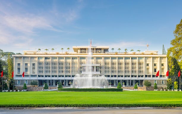 Independence Palace in Ho Chi Minh City with fountain and flags in front.