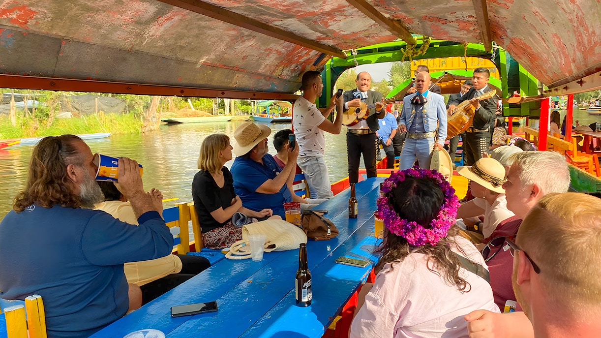 Guests on Trajinera party boat in Xochimilco, Mexico, enjoying vibrant canal tour.