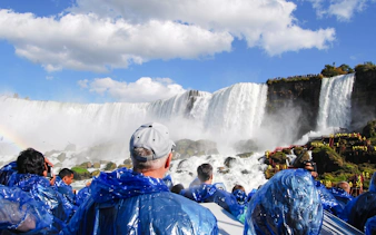 Visitors in blue ponchos viewing Niagara Falls from a boat tour in New York.