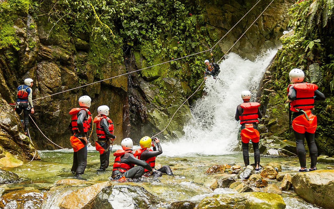 Group canyoning near waterfall in Braga, Portugal, with participants in helmets and life vests.
