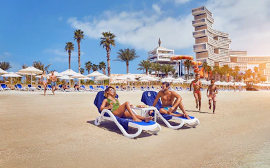 Visitors relaxing on the beach at Aquaventure Waterpark, Dubai, with slides and palm trees in the background.