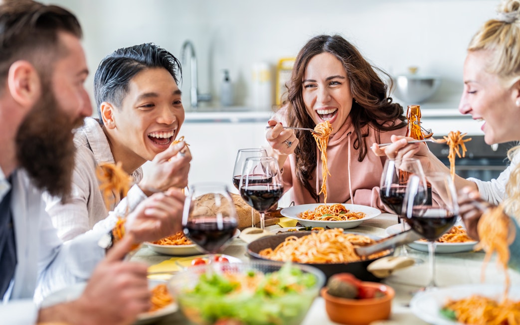 Friends enjoying pasta and wine together at a dining table.