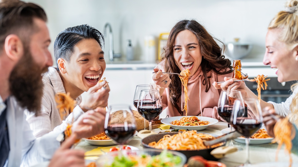 Friends enjoying pasta and wine together at a dining table.