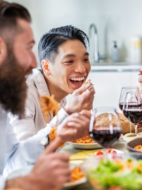 Friends enjoying pasta and wine together at a dining table.
