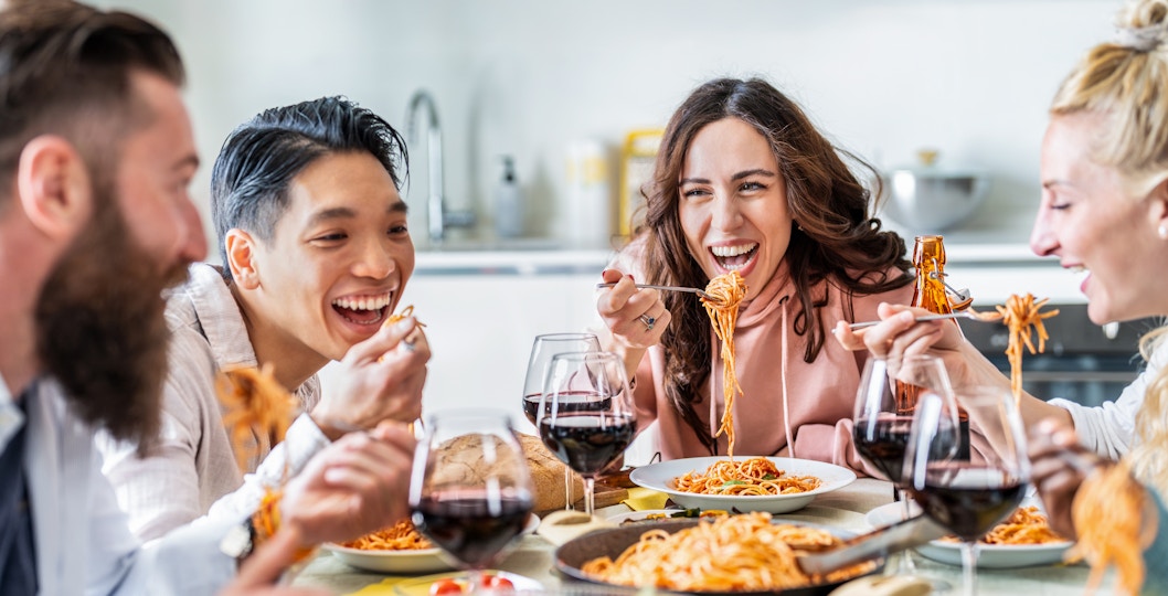 Friends enjoying pasta and wine together at a dining table.
