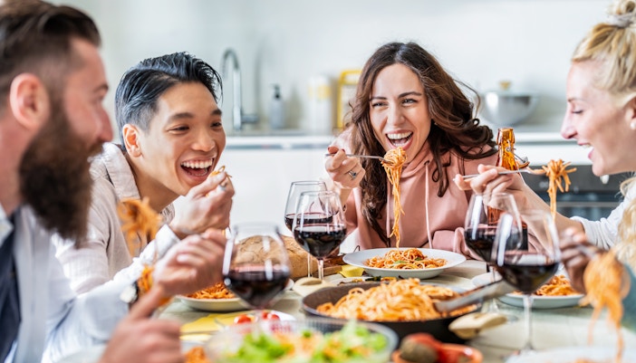Friends enjoying pasta and wine together at a dining table.