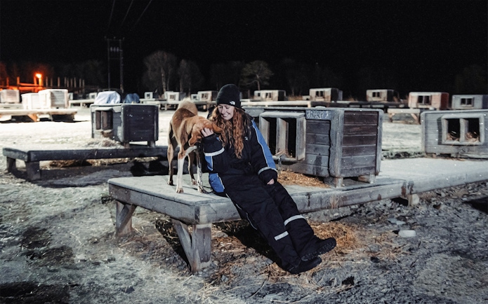 Woman interacting with Alaskan Husky at a dog sledding kennel at night.